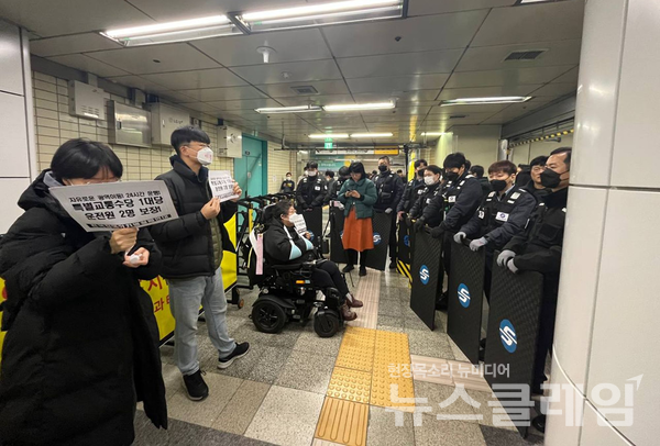 대합실 한 켠에서 침묵시위를 진행하고 있는 이형숙 대표 활동가와 그 앞을 방패로 둘러싸고 시민 통행을 방해하고 있는 서울교통공사 보안관 모습. 사진=전장연